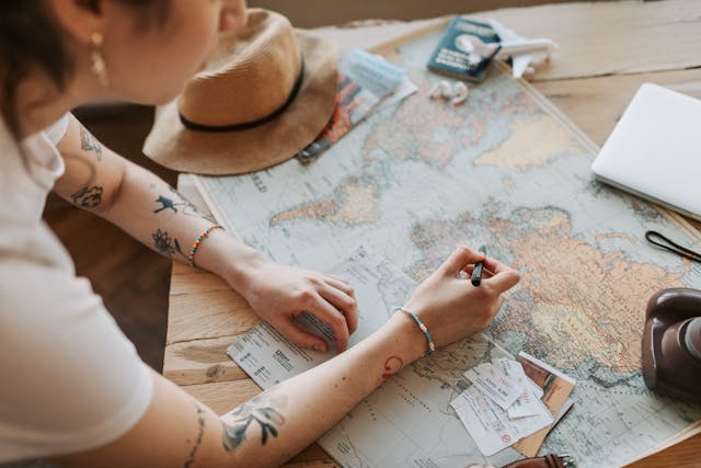 Woman planning a budget trip over a world map with a pen, hat and passport